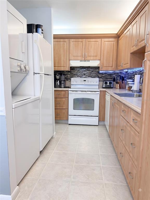 A kitchen features light wood cabinets, white appliances, a tiled backsplash, and a stacked laundry unit — 2530 BLACK OLIVE BOULEVARD, DELRAY BEACH, FL