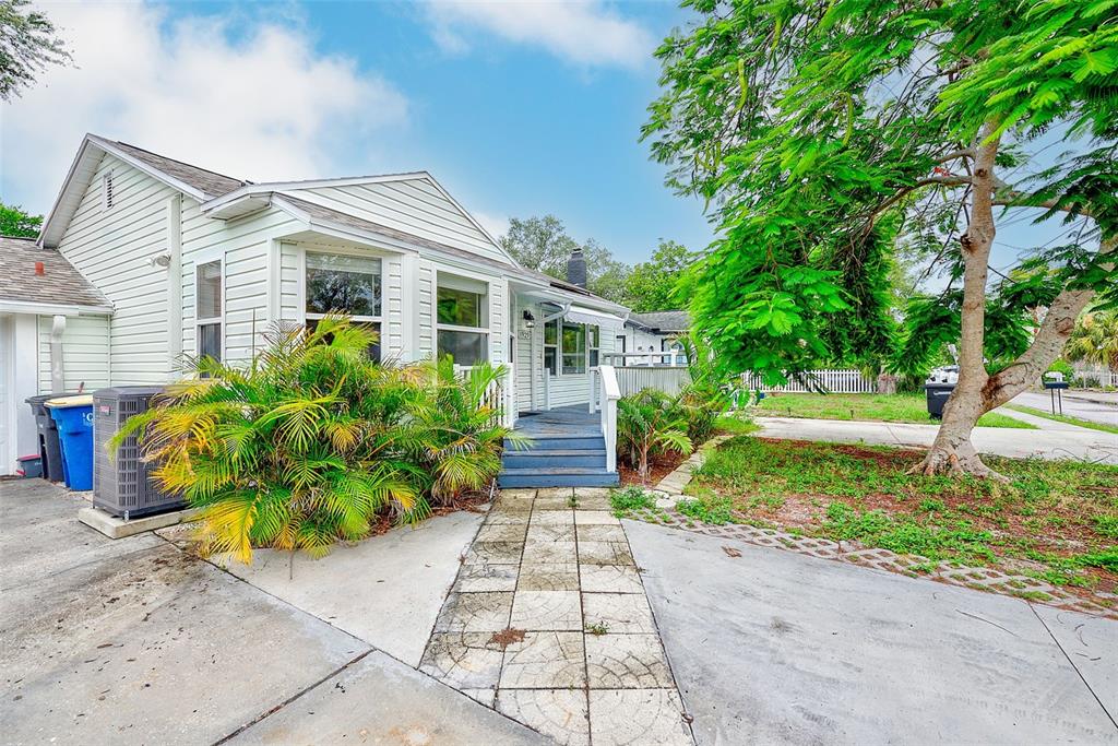 A light-colored house with a front porch, a paved walkway, and a large green tree — 1929 SPRINGTIME AVENUE, CLEARWATER, FL