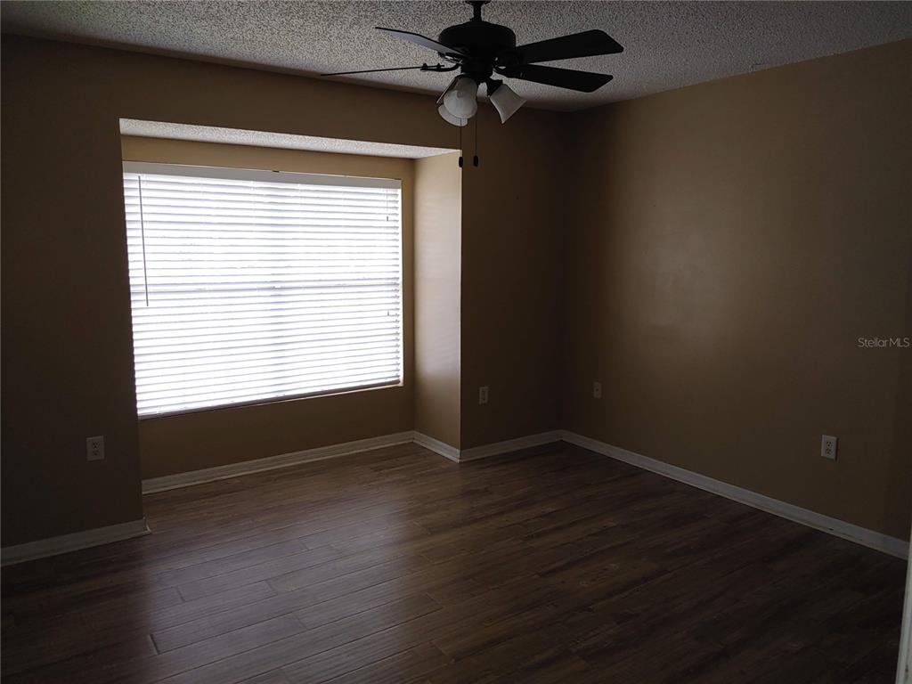 An empty room with brown walls, wood-look flooring, a ceiling fan, and a bay window — 215 LAKE BROOK CIRCLE UNIT 201, BRANDON, FL