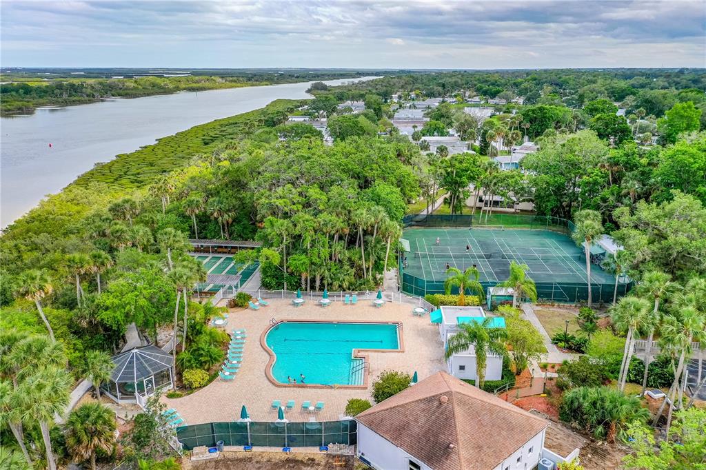 An aerial view shows a swimming pool, tennis courts, and lush trees near a river — 509 STARBOARD AVENUE, EDGEWATER, FL