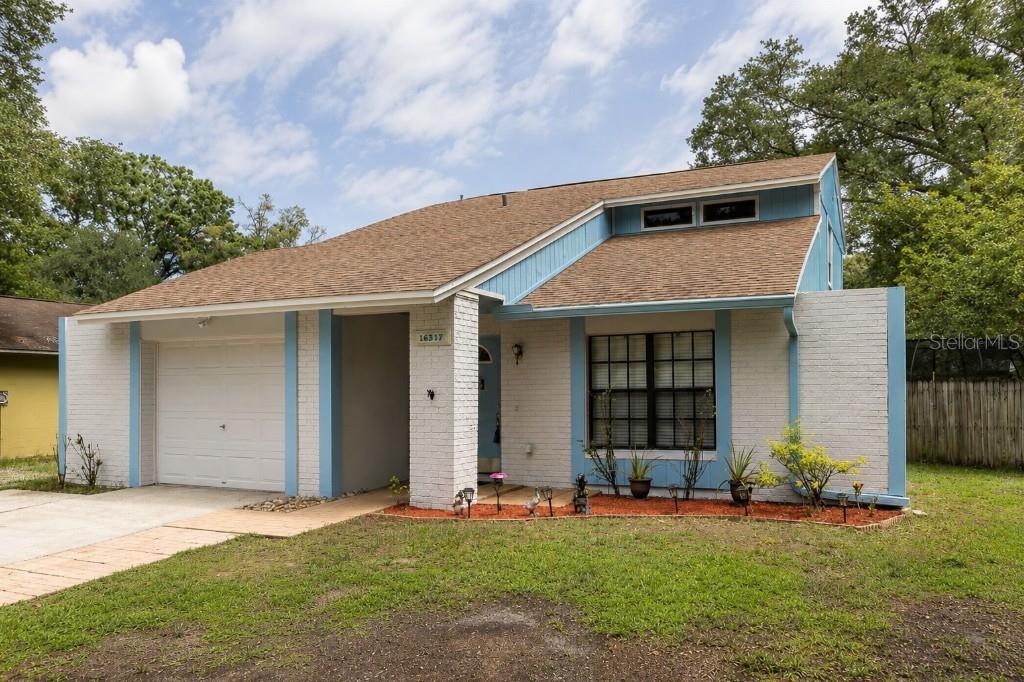 A single-story house with a white brick facade, blue trim, and an attached garage — 16317 CALIENTE PLACE, TAMPA, FL
