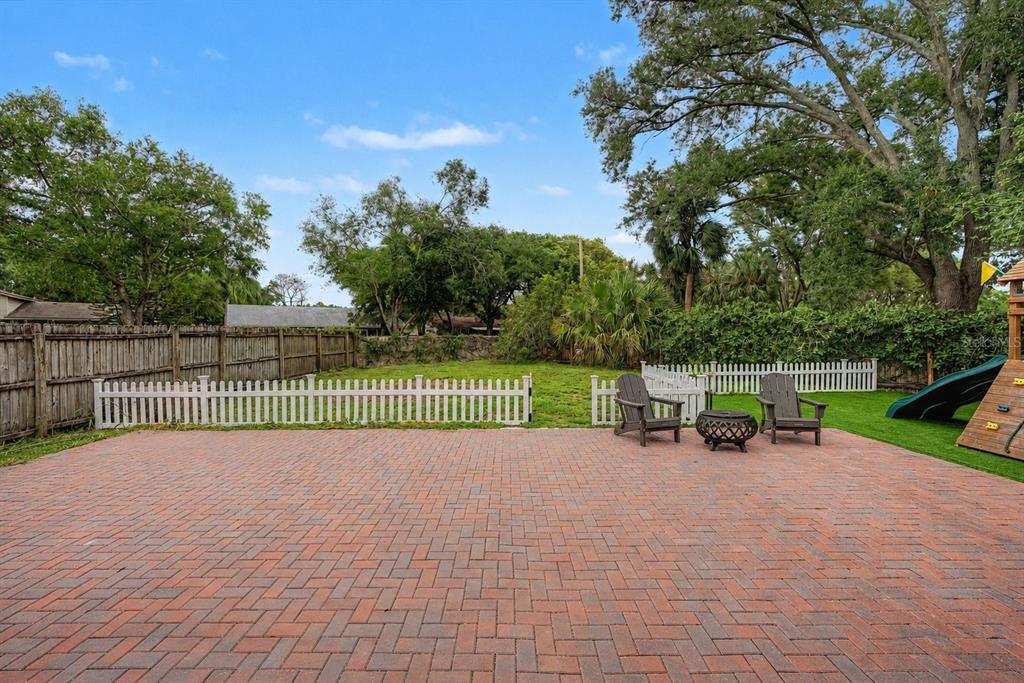 A brick patio overlooks a fenced backyard with two chairs and a fire pit — 16317 CALIENTE PLACE, TAMPA, FL