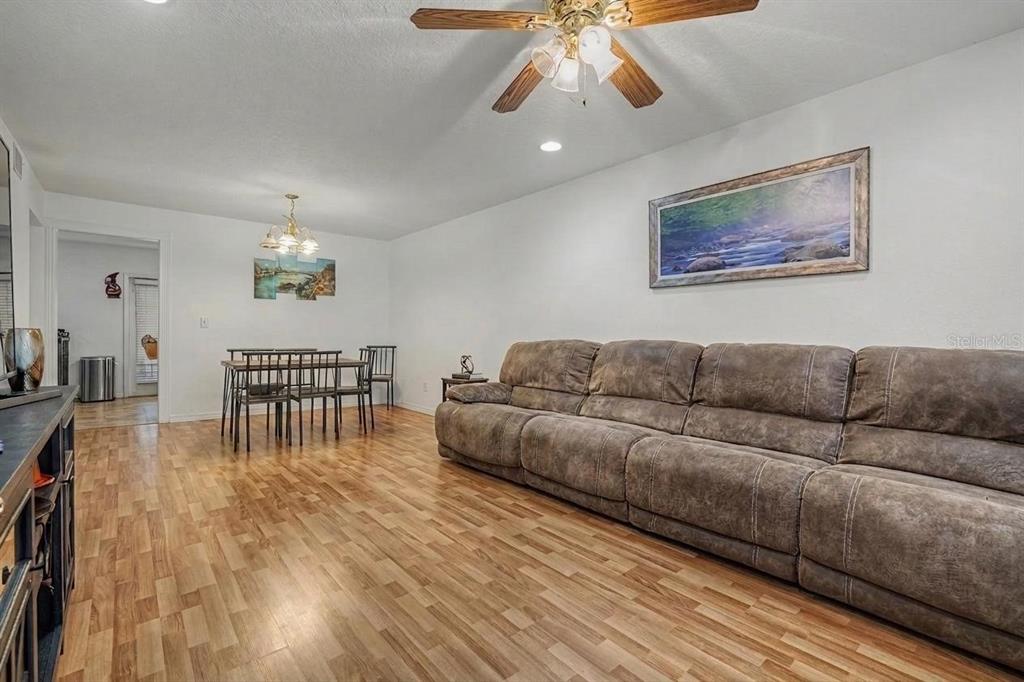 A living and dining area features a brown reclining sofa, wood-look flooring, and ceiling fans — 16317 CALIENTE PLACE, TAMPA, FL