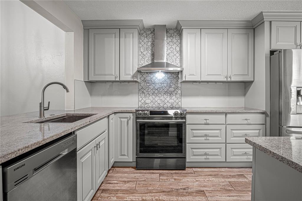 A kitchen features light gray cabinets, granite countertops, stainless steel appliances, and wood-look tile flooring — 138 FOX FIRE CIRCLE, DAYTONA BEACH, FL