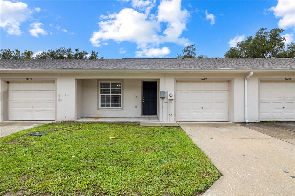 The exterior of a single-story townhouse features a garage, a front door, and a window — 37228 GRASSY HILL LANE, DADE CITY, FL