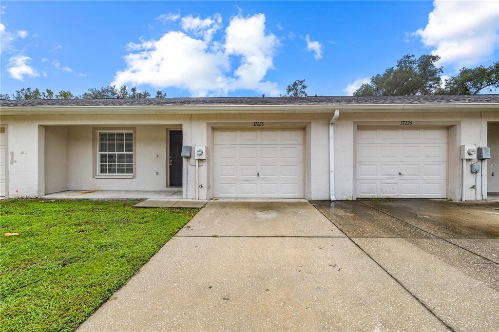 A single-story duplex features two garage doors, a front entrance, and a concrete driveway — 37228 GRASSY HILL LANE, DADE CITY, FL