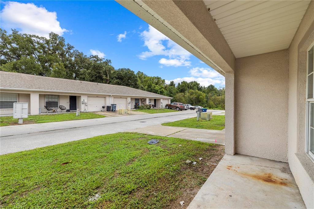 A view from a covered concrete porch looking out toward a row of townhomes — 37228 GRASSY HILL LANE, DADE CITY, FL
