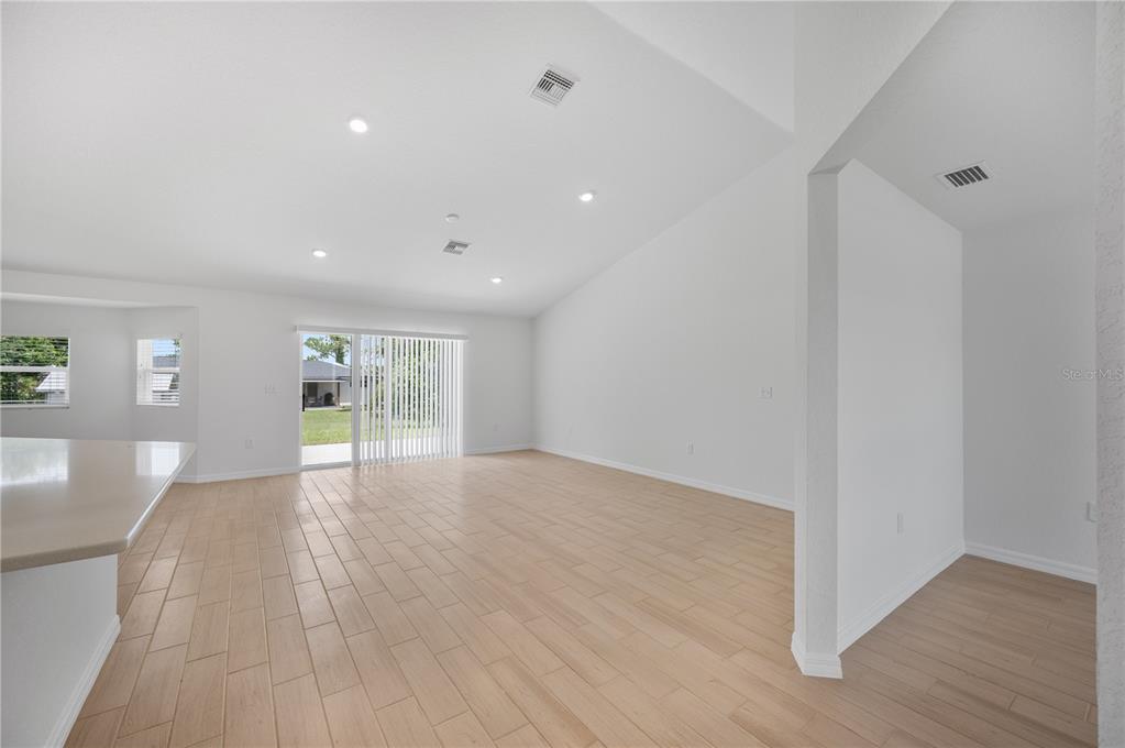 An open-concept living area features light wood-look tile flooring, vaulted ceilings, and sliding glass doors — 1708 MANATEE DRIVE, SEBRING, FL
