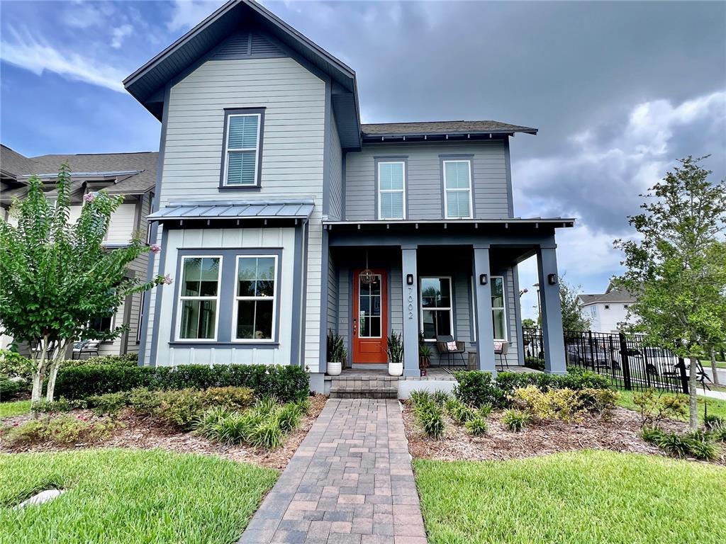 A two-story house features gray siding, a covered front porch, and a bright orange door — 7002 ARNOLDSON STREET, ORLANDO, FL