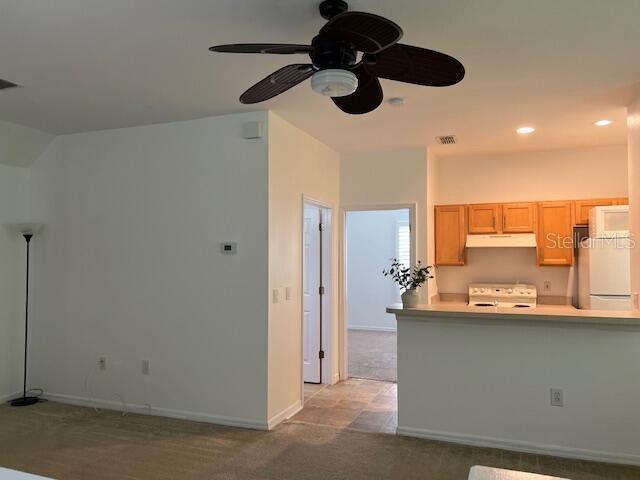 A living room with beige carpet and a ceiling fan opens to a kitchen with cabinets — 947 SPRING PARK LOOP APT B, KISSIMMEE, FL