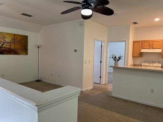 An interior view shows a carpeted living area with a ceiling fan and an adjacent kitchen — 947 SPRING PARK LOOP APT B, KISSIMMEE, FL