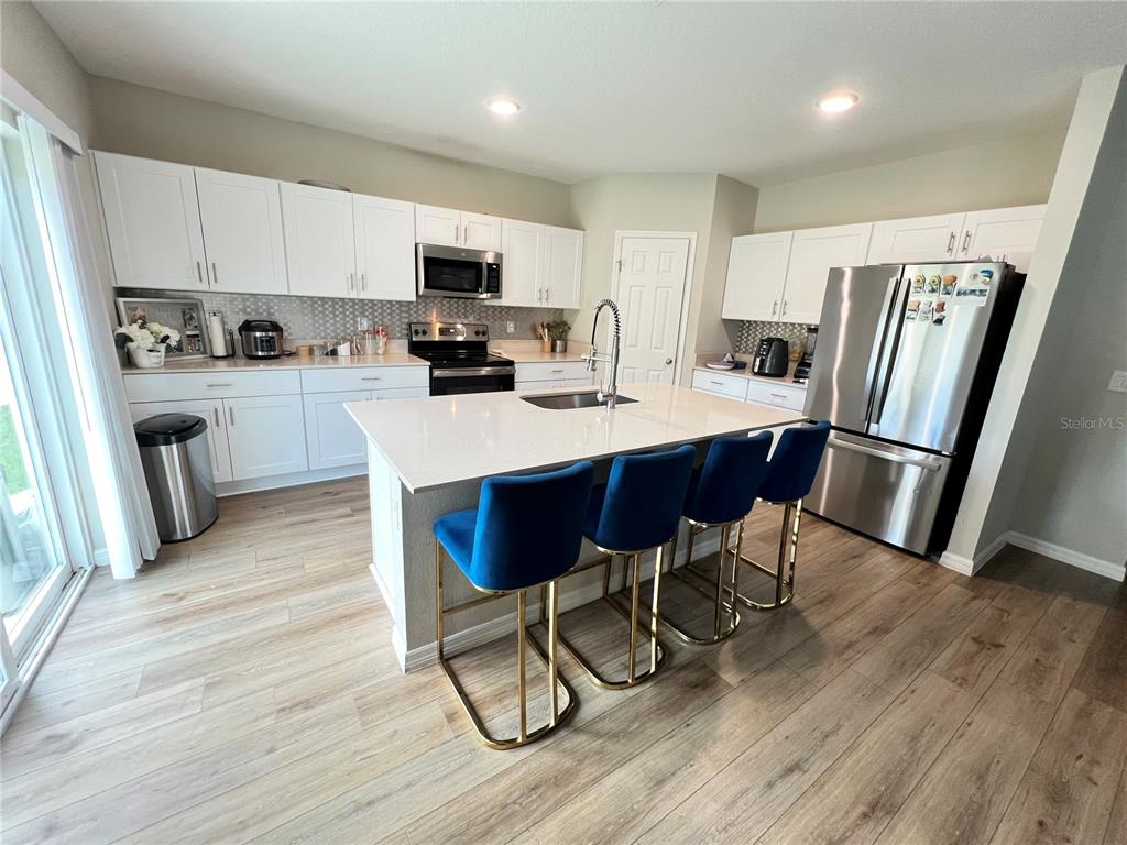 A kitchen features white cabinets, stainless steel appliances, a quartz island, and blue bar stools — 5377 MADDIE DRIVE, HAINES CITY, FL