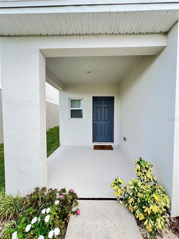 A covered concrete entryway leads to a dark blue front door and a small window — 5377 MADDIE DRIVE, HAINES CITY, FL