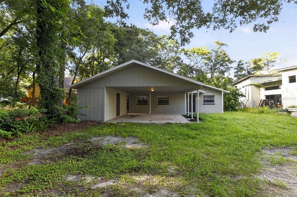 A house exterior features a large attached carport and a grassy yard with surrounding trees — 26430 SLEEPY HOLLOW STREET, MOUNT PLYMOUTH, FL