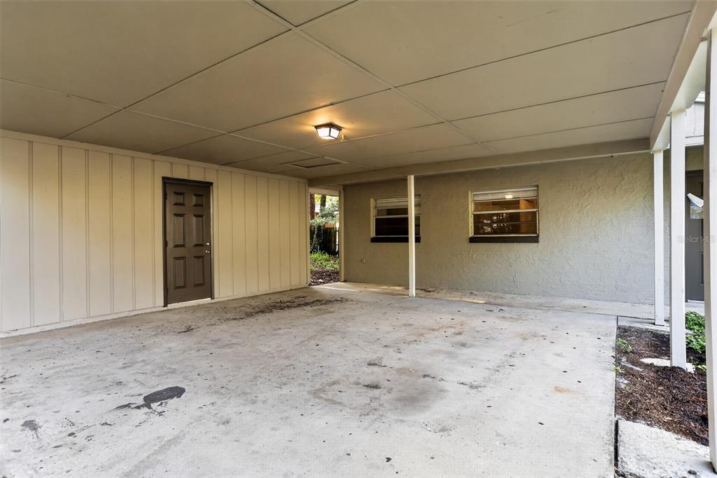 A concrete carport features a brown door, two windows, and a ceiling-mounted light fixture — 26430 SLEEPY HOLLOW STREET, MOUNT PLYMOUTH, FL