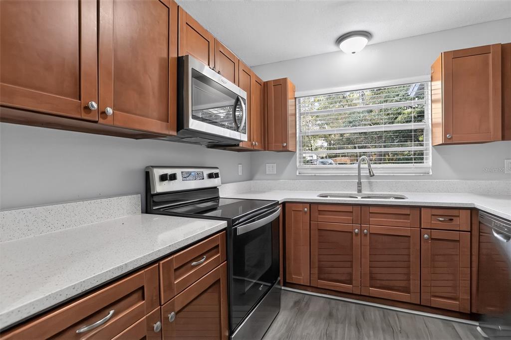 A kitchen features wood cabinets, stainless steel appliances, white countertops, and a window above the sink — 26430 SLEEPY HOLLOW STREET, MOUNT PLYMOUTH, FL