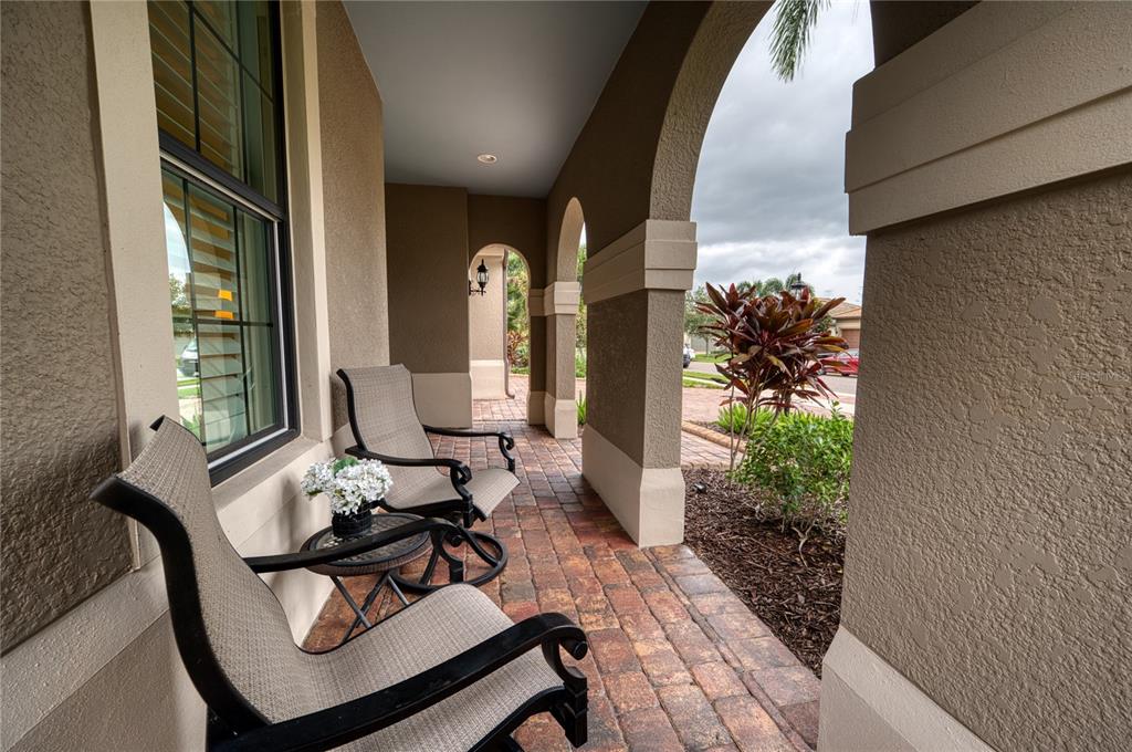 A covered outdoor patio features arched columns, brick pavers, and two chairs with a small table — 16918 LOUDON PLACE, BRADENTON, FL
