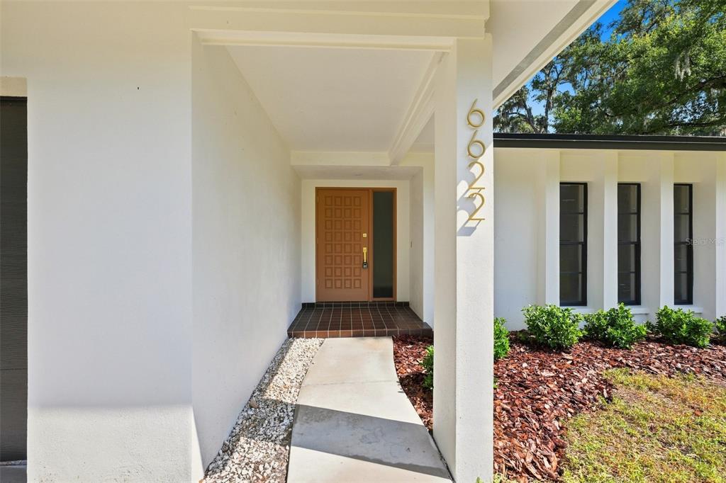 A concrete walkway leads to a front door with a grid-patterned design and sidelight — 6622 GLENCOE DRIVE, TEMPLE TERRACE, FL