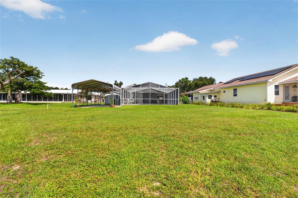 A large grassy backyard features a screened-in pool enclosure and a detached metal carport — 148 N LAKE REEDY BOULEVARD, FROSTPROOF, FL