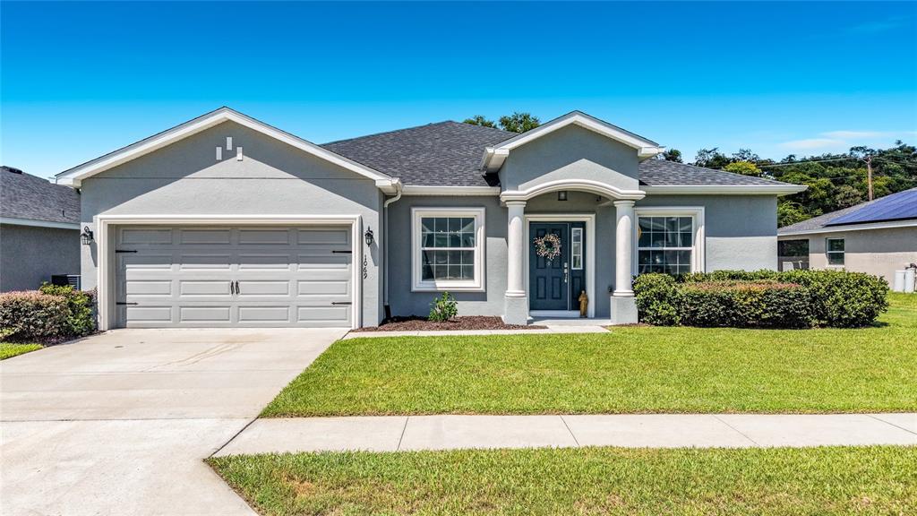 A single-story gray house features a two-car garage, a covered entryway with columns, and landscaping — 1069 SANDPIPER LOOP, WINTER HAVEN, FL