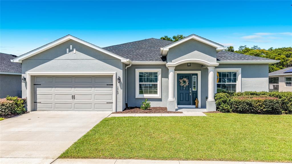 A single-story gray house features a two-car garage, a covered entryway with columns, and landscaping — 1069 SANDPIPER LOOP, WINTER HAVEN, FL