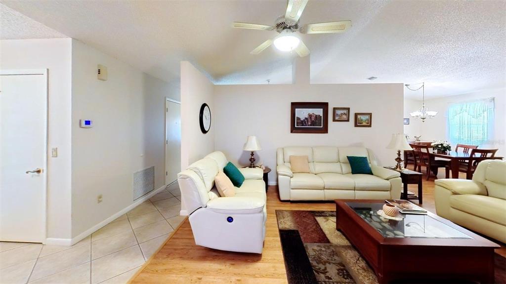 A living room features light-colored leather sofas, a wooden coffee table, and a ceiling fan — 1410 NEW ABBEY AVENUE, LEESBURG, FL