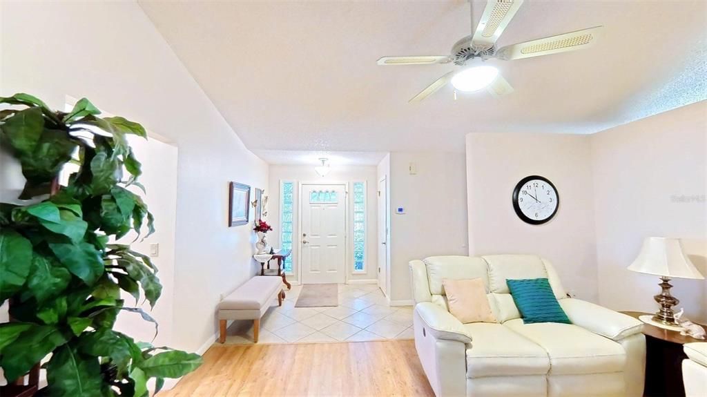 A living room features a white sofa, a ceiling fan, and a front entryway — 1410 NEW ABBEY AVENUE, LEESBURG, FL