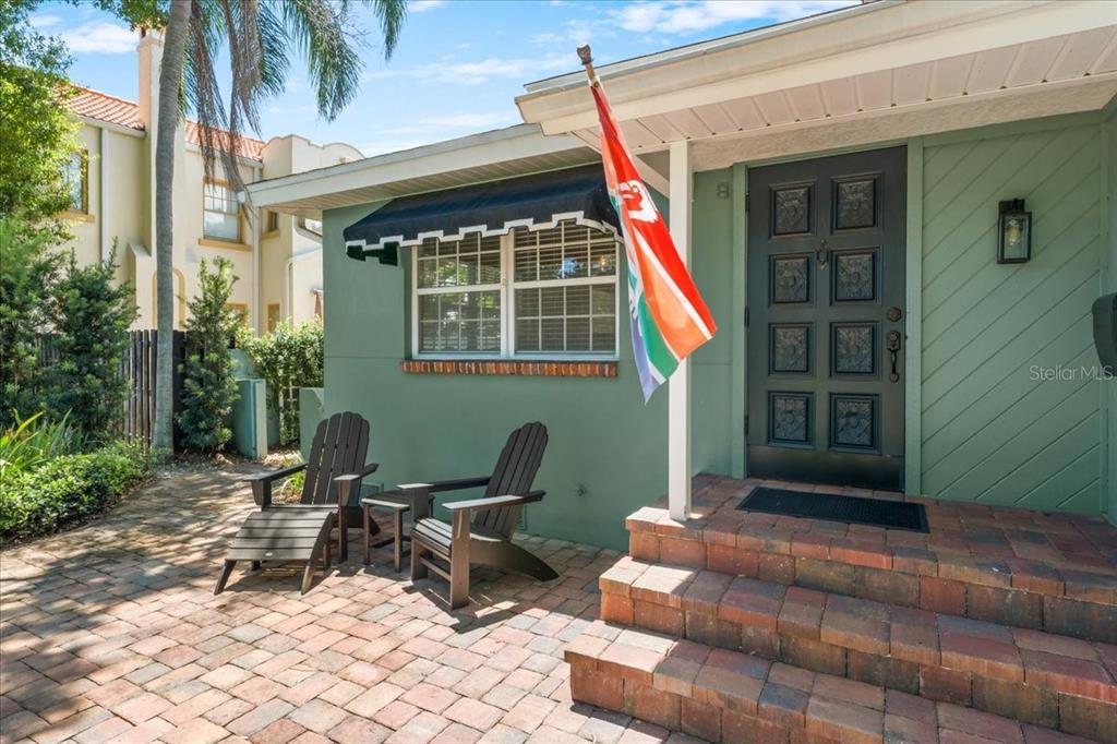 A green house exterior features a brick patio, two dark chairs, and a front door — 3528 FOSTER HILL DRIVE N, ST PETERSBURG, FL