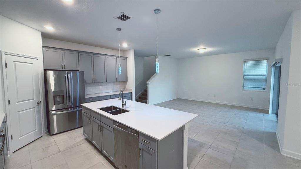 A kitchen with gray cabinets, a white island, and stainless steel appliances opens to a living area — 11830 LANGUAGE WAY, ORLANDO, FL