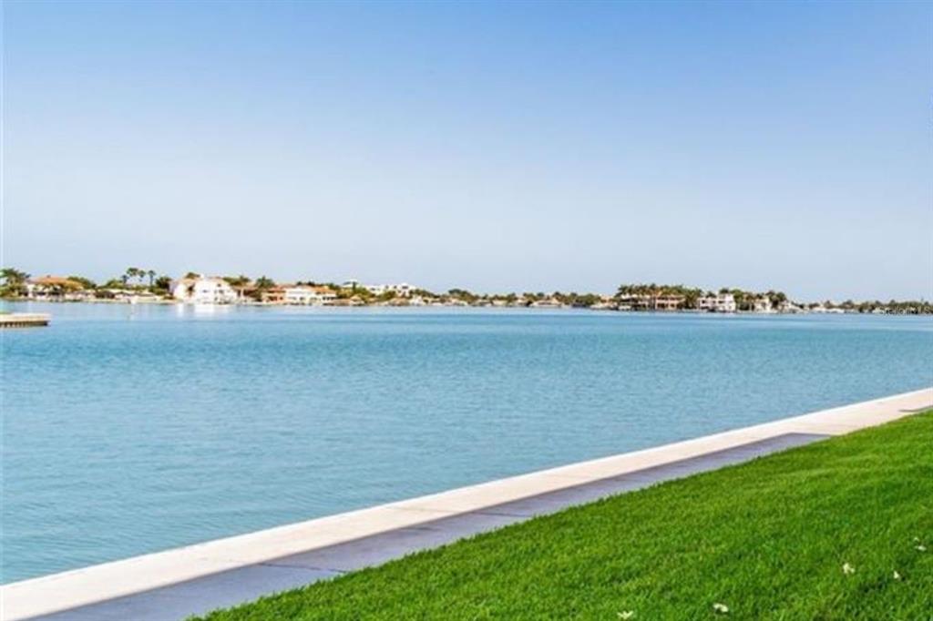 A grassy lawn borders a concrete seawall overlooking a wide bay with distant waterfront homes — 7560 BAY ISLAND DRIVE S UNIT 146, SOUTH PASADENA, FL