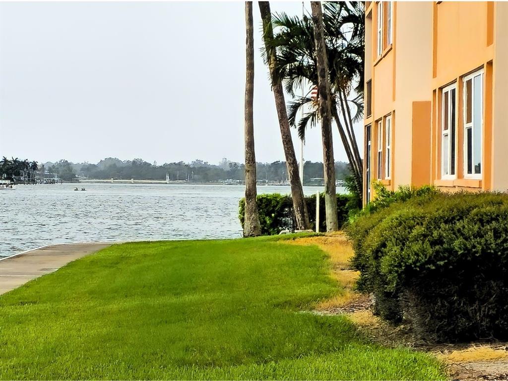 A grassy lawn borders a waterfront area next to a multi-story peach-colored building — 7560 BAY ISLAND DRIVE S UNIT 146, SOUTH PASADENA, FL