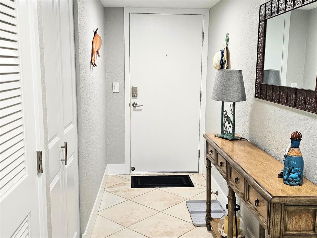 An entryway features a white door, a wooden console table, a lamp, and tiled flooring — 7560 BAY ISLAND DRIVE S UNIT 146, SOUTH PASADENA, FL