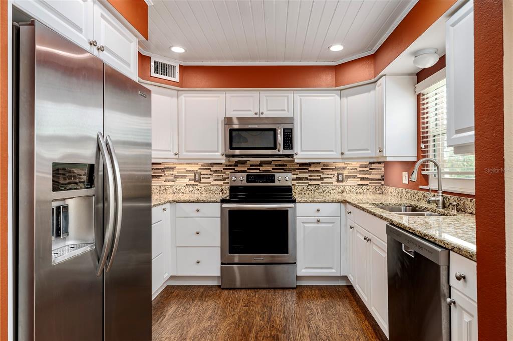 A kitchen features white cabinets, stainless steel appliances, granite countertops, and a tile backsplash — 7001 PLACE DE LA PAIX UNIT 2A, SOUTH PASADENA, FL