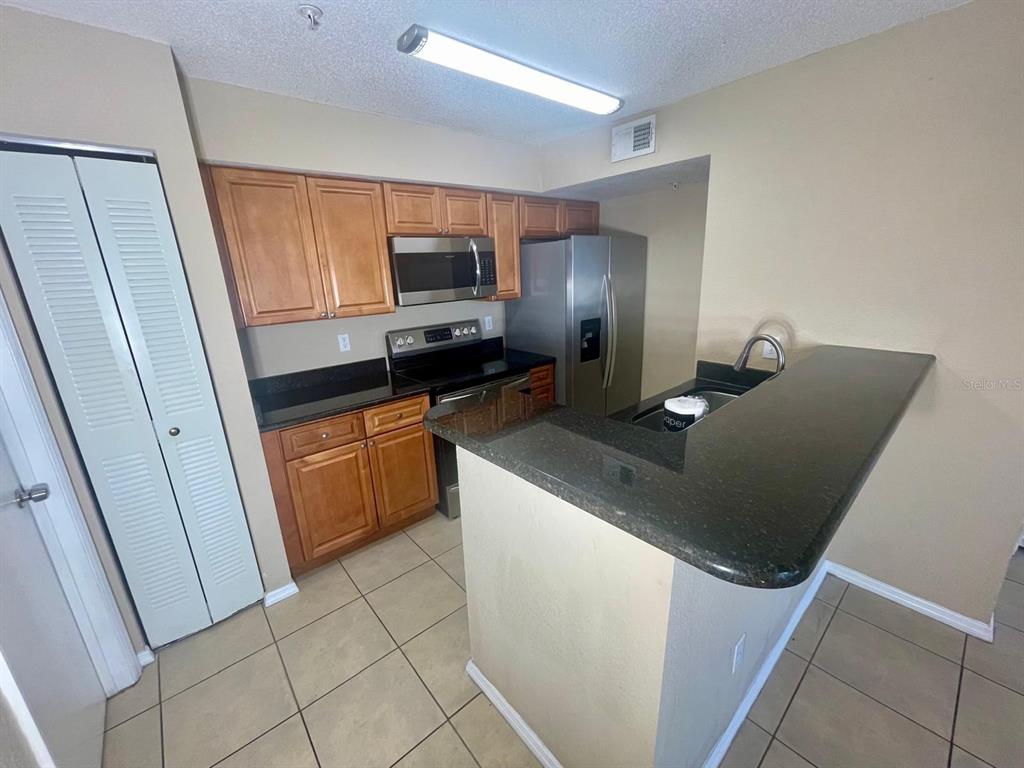 A kitchen with wooden cabinets, stainless steel appliances, and a dark countertop breakfast bar — 4103 TROPICAL ISLE BOULEVARD UNIT 138, KISSIMMEE, FL