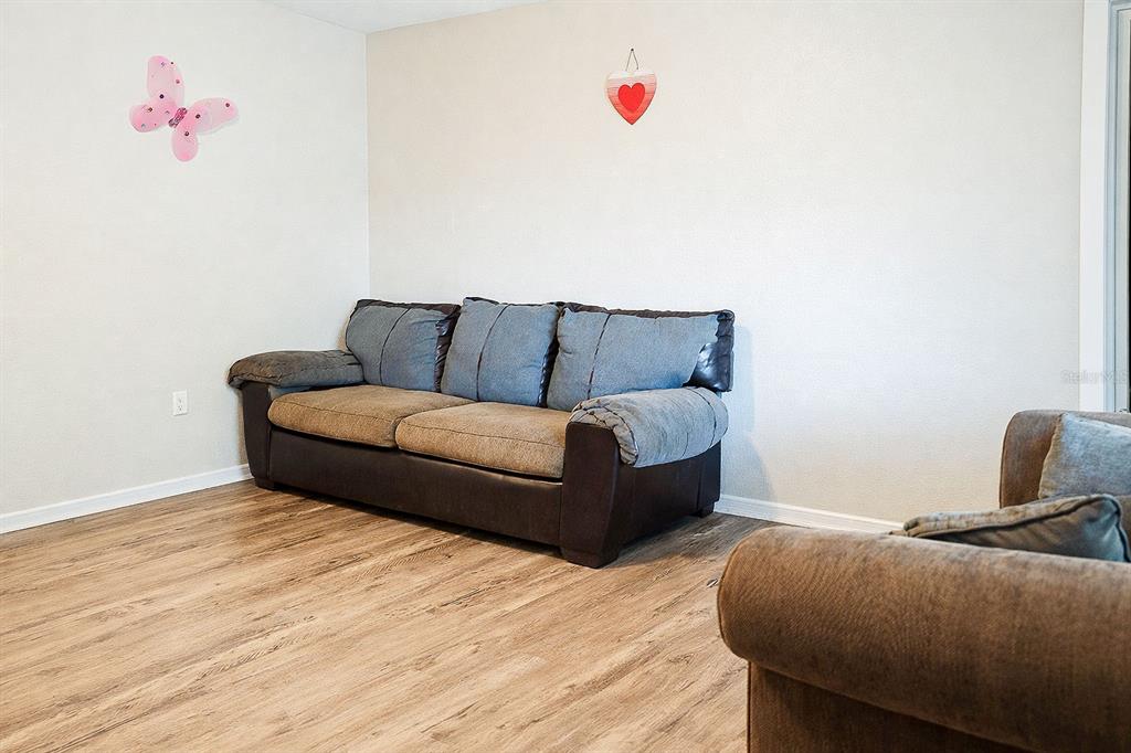 A living room features wood-look flooring, a brown and blue sofa, and wall decorations — 473 WURST RD, OCOEE, FL