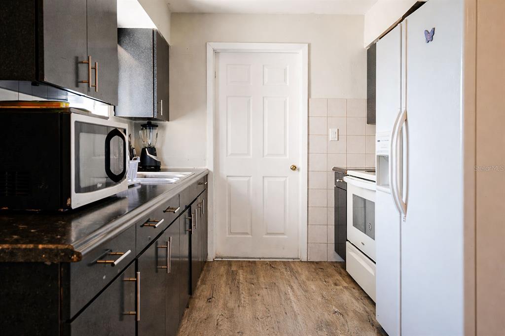 A kitchen with dark cabinets, black countertops, white appliances, and a white door — 473 WURST RD, OCOEE, FL