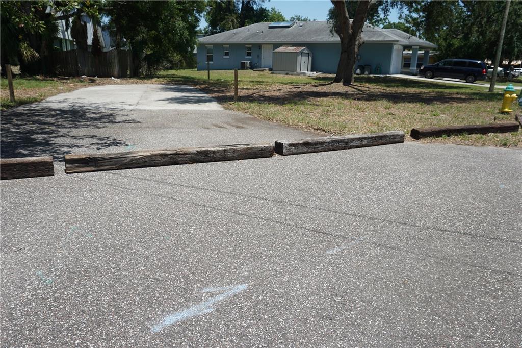 A paved parking area features wooden wheel stops in front of a blue house — 0 74TH AVENUE N, PINELLAS PARK, FL