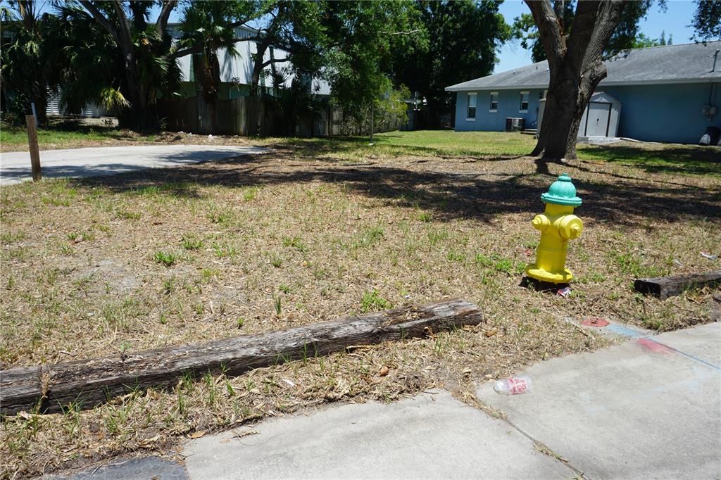 A yellow fire hydrant sits on a grassy lot next to a sidewalk and house — 0 74TH AVENUE N, PINELLAS PARK, FL