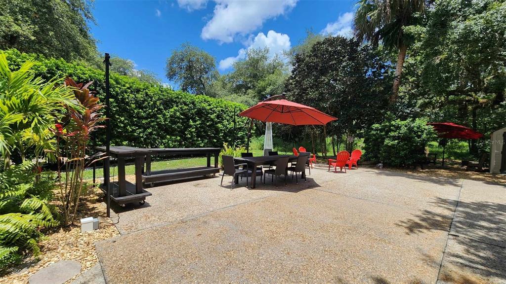 A concrete patio features a dining set with a red umbrella and outdoor bar furniture — 389 LONGHORN DRIVE, RIVER RANCH, FL