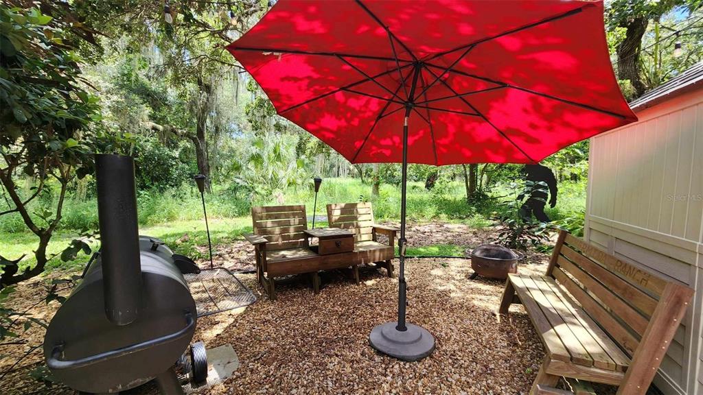 A gravel patio features a red umbrella, wooden benches, and a large smoker grill — 389 LONGHORN DRIVE, RIVER RANCH, FL