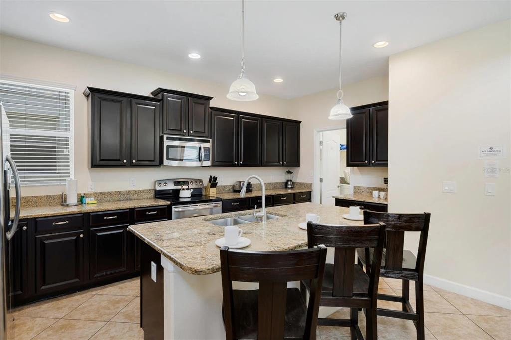 A kitchen features dark wood cabinets, granite countertops, a center island, and tile flooring — 2995 BUCCANEER PALM ROAD, KISSIMMEE, FL
