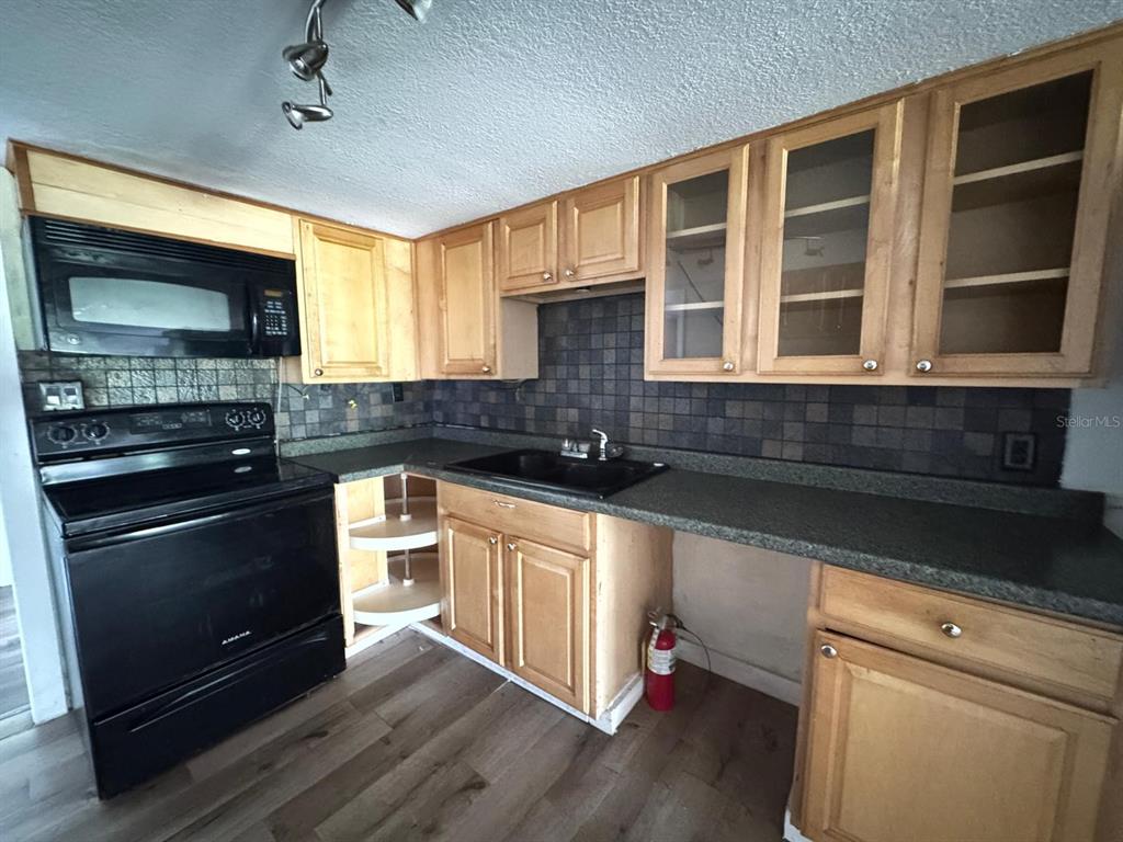 A kitchen features light wood cabinets, black appliances, a dark tiled backsplash, and laminate flooring — 224 10TH AVENUE, OCOEE, FL