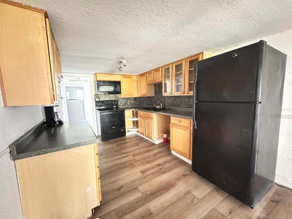 A kitchen features light wood cabinets, black appliances, dark countertops, and wood-look flooring — 224 10TH AVENUE, OCOEE, FL