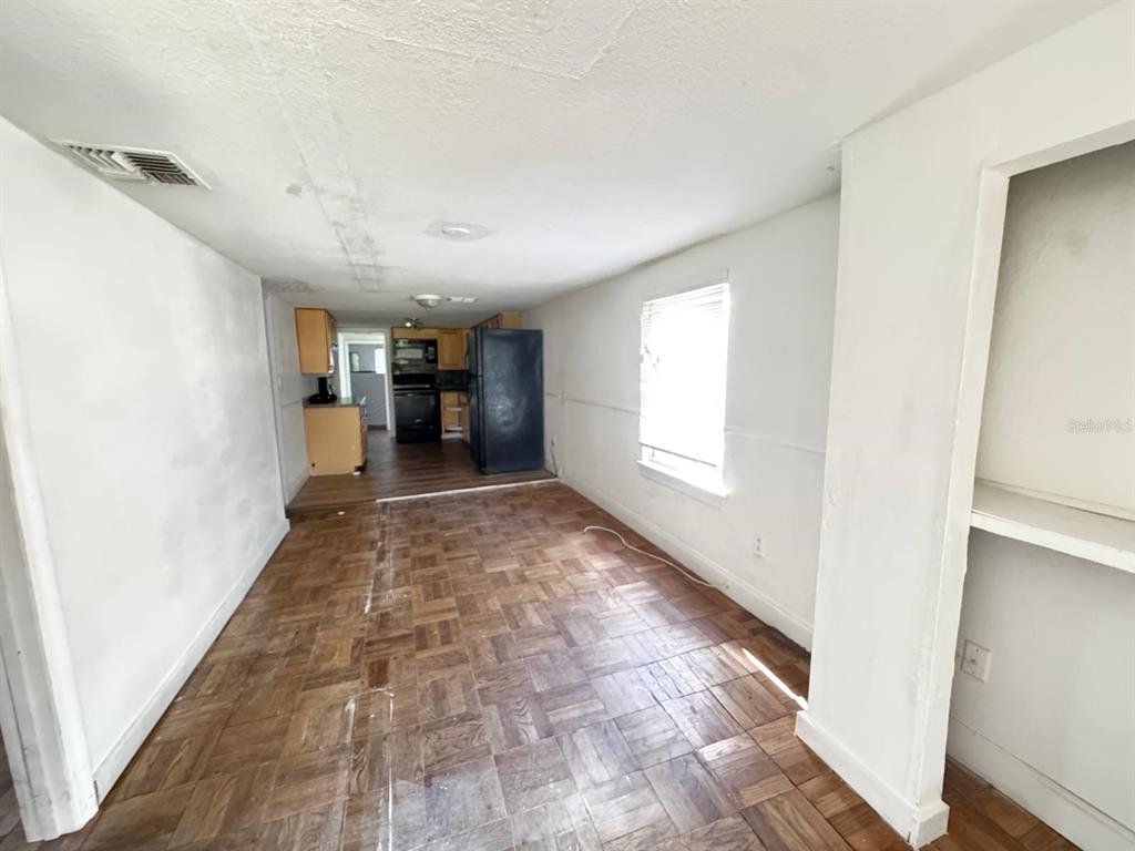 A room with parquet wood flooring leads to a kitchen with dark appliances and cabinets — 224 10TH AVENUE, OCOEE, FL