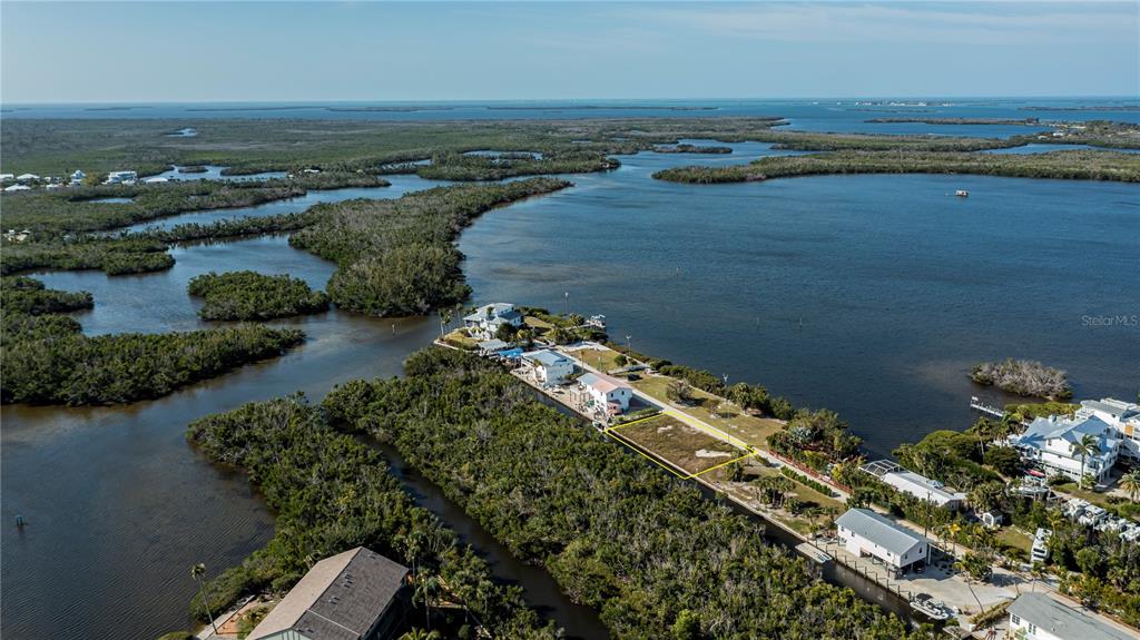 An aerial view shows a vacant waterfront lot outlined in yellow near several coastal houses — 8153 MOYER LANE, BOKEELIA, FL