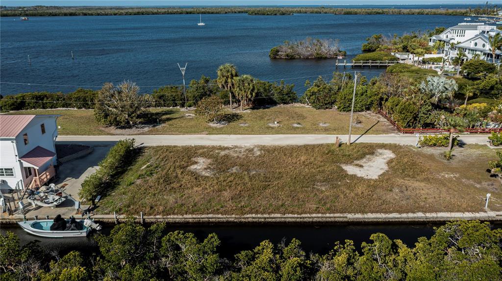 An aerial view shows a vacant waterfront lot with a canal and a nearby house — 8153 MOYER LANE, BOKEELIA, FL