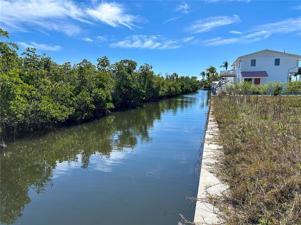 A narrow canal flows between a dense mangrove thicket and a residential property with landscaping — 8153 MOYER LANE, BOKEELIA, FL