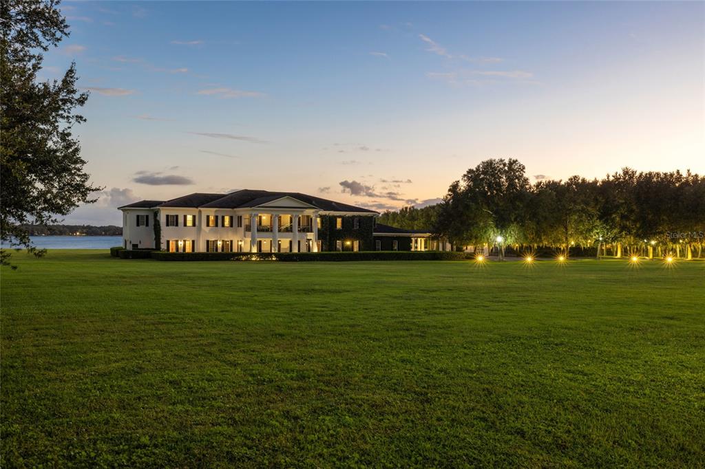 A large white two-story mansion sits on a vast green lawn beside a lake — 9508 WINDY RIDGE ROAD, WINDERMERE, FL