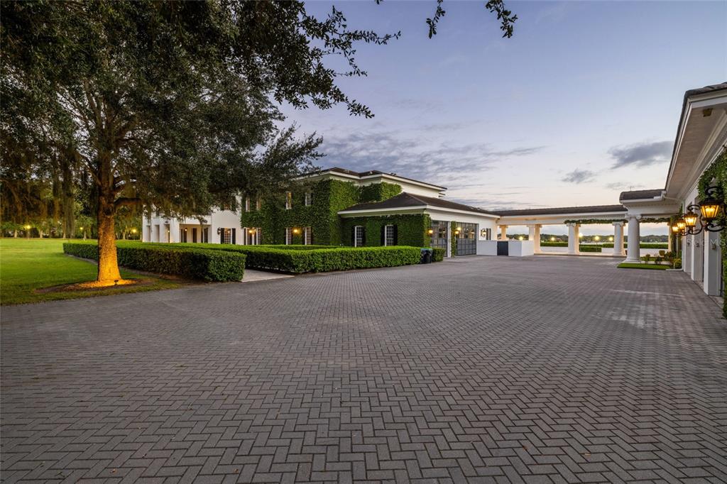 A large white house with ivy-covered walls and a paved driveway at dusk — 9508 WINDY RIDGE ROAD, WINDERMERE, FL