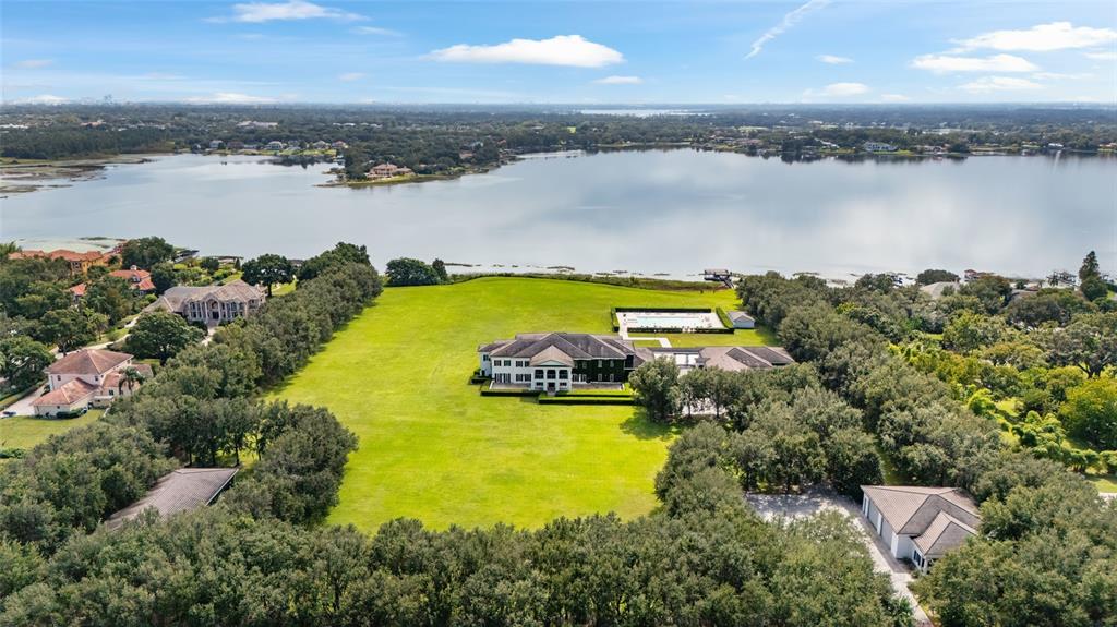 An aerial view shows a large house with a pool on a grassy waterfront lot — 9508 WINDY RIDGE ROAD, WINDERMERE, FL